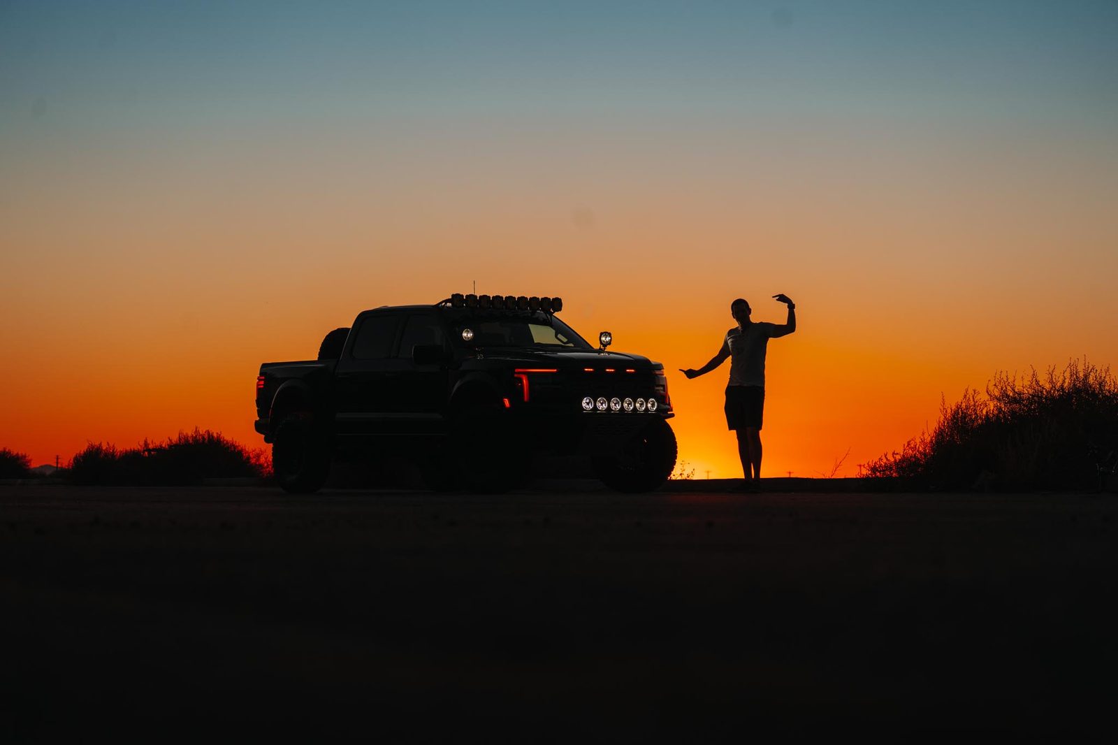 A person and an off-road truck in silhouette against an orange sunset.